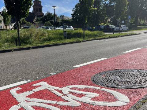 Auf der Straße ist ein roter Streifen markiert. Ein Fahrrad-Symbol zeigt, dass der Streifen für Fahrräder ist. 