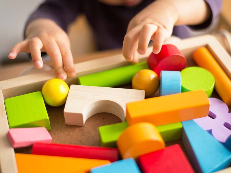 Zwei Kinderhände greifen in eine Holzbox voller bunter Holzbausteine.