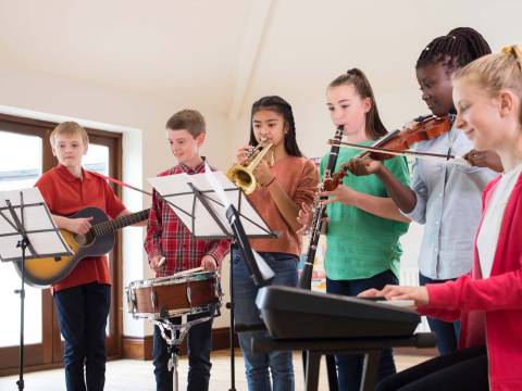 Sechs Kinder spielen in einer Musikschule verschiedene Instrumente, zum Beispiel Gitarre, Trommel, Keyboard.