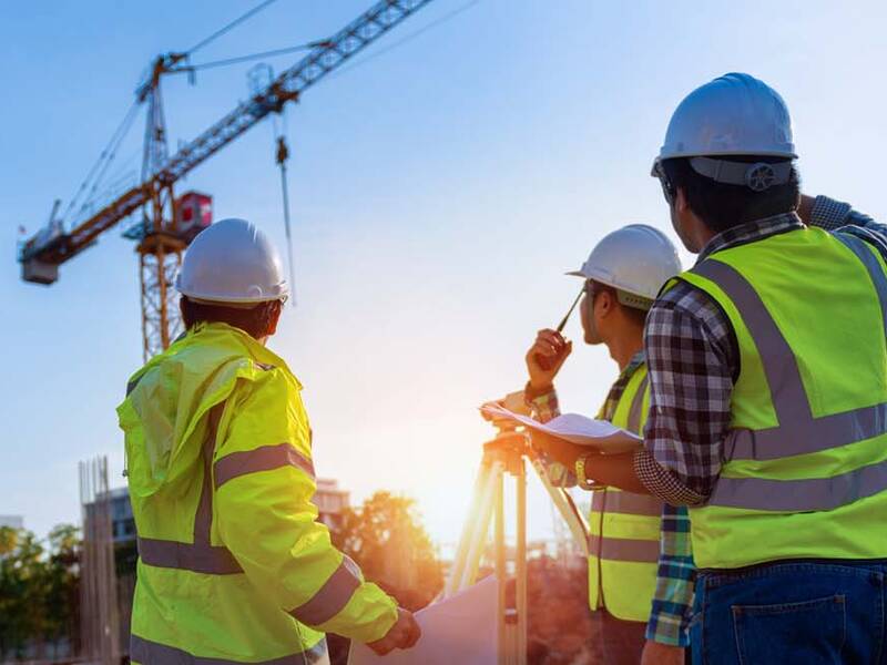 Drei Bauarbeiter in Warnwesten blicken auf einen Baukran.