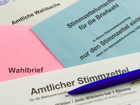 Ein Kugelschreiber liegt auf rosa, hellblau und cremfarbenen Briefwahlunterlagen.